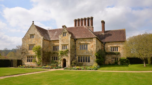 Jacobean sandstone house with front flower borders and lawn in spring at Bateman's